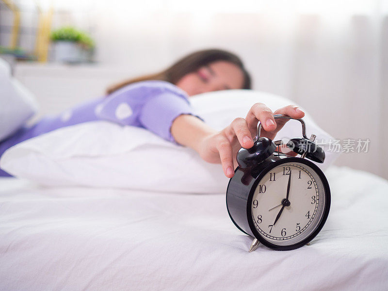 The sleepy woman sleeping in bed, using the hand to press the alarm clock in the morning. Good morning on a lazy day